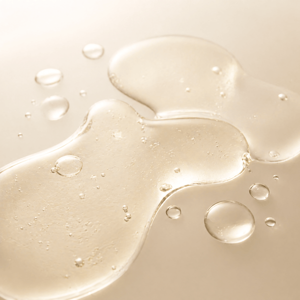 Translucent liquid droplets spreading evenly to represent kojic acid for skin brightening and tone clarity